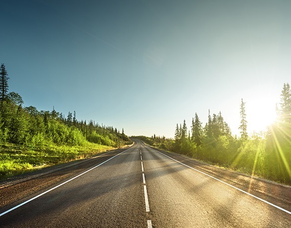 Road surrounded by trees with sunrise